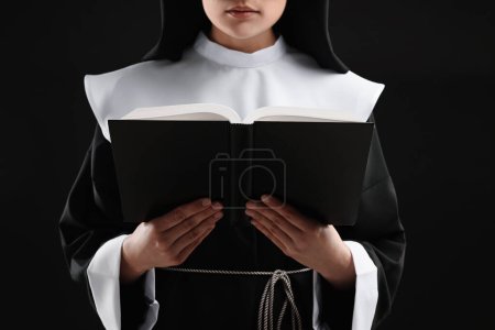 Téléchargez les photos : Nonne lecture de la Bible sur fond noir, gros plan - en image libre de droit