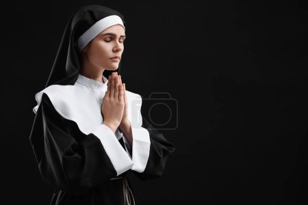 Monja con las manos cerradas rezando a Dios sobre fondo negro. Espacio para texto