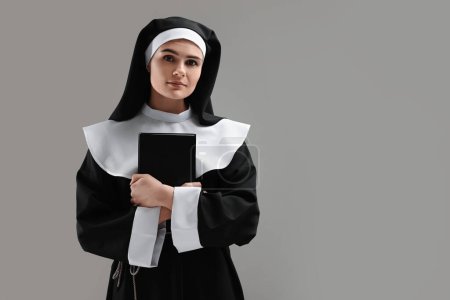 Nun with Bible on grey background, space for text