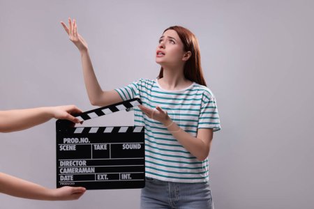 Foto de Actriz emocional interpretando el papel mientras la segunda asistente de cámara sostiene el clapperboard sobre fondo gris - Imagen libre de derechos