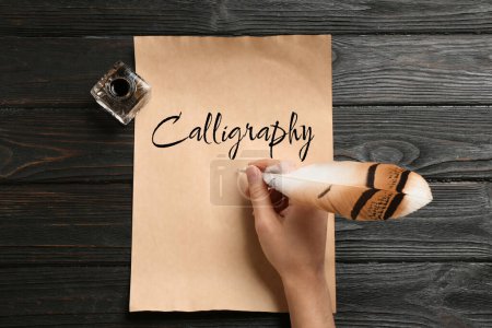 Photo for Woman writing word Calligraphy with feather and ink on parchment at wooden table, top view - Royalty Free Image