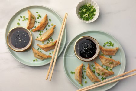 Téléchargez les photos : Délicieux gyoza (boulettes asiatiques) avec sauce soja, oignons verts et baguettes sur table blanche, plat - en image libre de droit