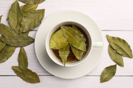 Téléchargez les photos : Tasse de thé fraîchement infusé avec des feuilles de laurier sur une table en bois blanc, plat - en image libre de droit