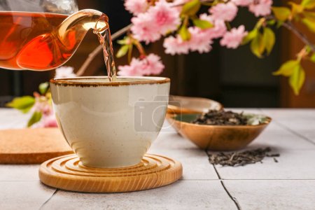 Traditional ceremony. Pouring brewed tea from teapot into cup on tiled table, closeup