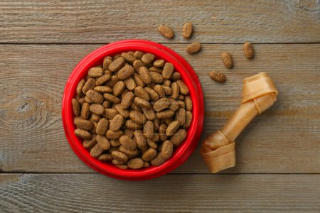 Dry dog food and treat (chew bone) on wooden floor, flat lay