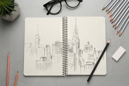 Stadtbild-Skizze in Notizbuch, Bleistift, Radiergummi und Brille auf grauem Tisch, flach gelegt