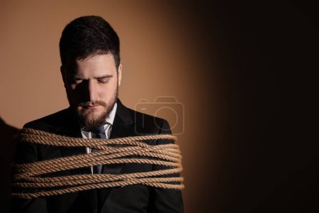 Man tied up and taken hostage on dark background. Space for text