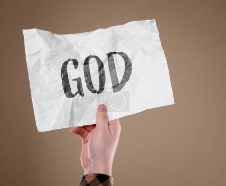 Téléchargez les photos : Homme tenant du papier froissé avec le mot Dieu sur fond brun pâle, gros plan - en image libre de droit