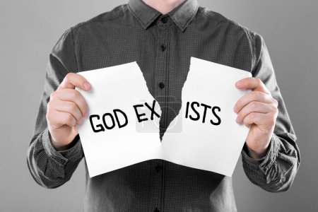 Photo for Atheism as religious position. Man ripping sheet of paper with text God Exists on grey background, closeup - Royalty Free Image