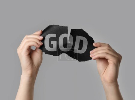 Atheism as religious position. Woman ripping black paper with word God on light grey background, closeup