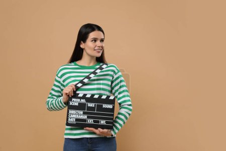 Foto de Feliz actriz con clapperboard sobre fondo beige, espacio para el texto. Industria cinematográfica - Imagen libre de derechos