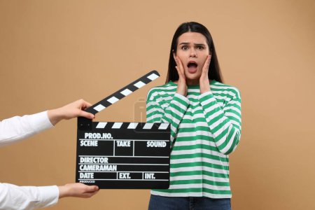 Foto de Actriz emocional actuando mientras la segunda cámara asistente sostiene el clapperboard sobre fondo beige. Industria cinematográfica - Imagen libre de derechos