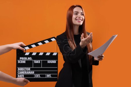 Foto de Actriz desempeñando el papel mientras que la segunda cámara asistente sostiene clapperboard sobre fondo naranja, enfoque selectivo - Imagen libre de derechos