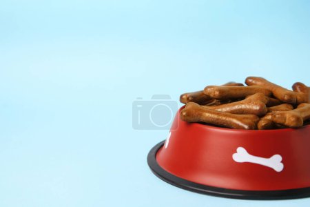 Téléchargez les photos : Bol rouge avec biscuits pour chien en forme d'os sur fond bleu clair, gros plan. Espace pour le texte - en image libre de droit