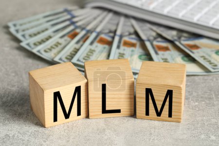 Téléchargez les photos : Marketing multi-niveaux. Abréviation MLM de cubes avec lettres et billets en dollars sur table grise - en image libre de droit