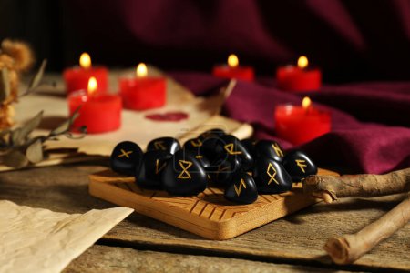 Many black rune stones and burning candles on wooden table, closeup