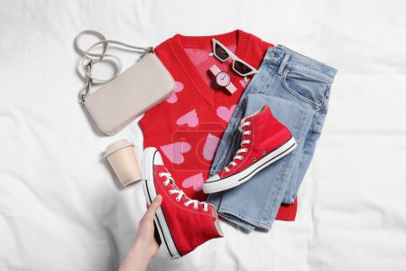 Foto de Mujer sosteniendo nuevas zapatillas rojas con estilo, accesorios, taza de bebida y ropa en tela blanca, vista superior. Traje casual - Imagen libre de derechos