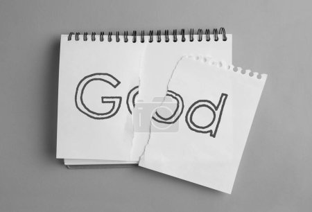 Téléchargez les photos : L'athéisme comme position religieuse. Papier déchiré avec le mot Dieu dans le carnet sur fond gris, vue du dessus - en image libre de droit