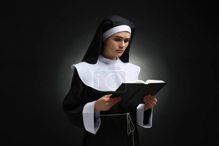 Foto de Joven monja leyendo la Biblia sobre fondo negro - Imagen libre de derechos
