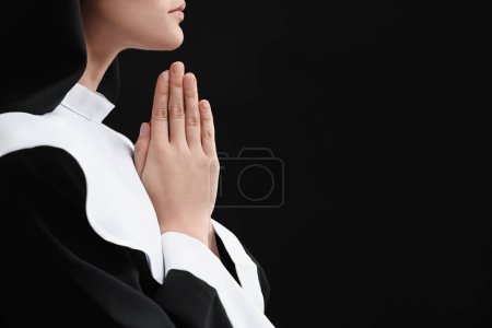 Téléchargez les photos : Nonne avec les mains jointes priant Dieu sur fond noir, gros plan. Espace pour le texte - en image libre de droit