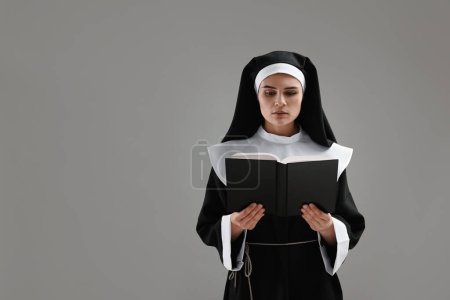 Téléchargez les photos : Nonne lecture de la Bible sur fond gris, espace pour le texte - en image libre de droit