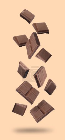 Pedazos de barra de chocolate cayendo sobre fondo beige