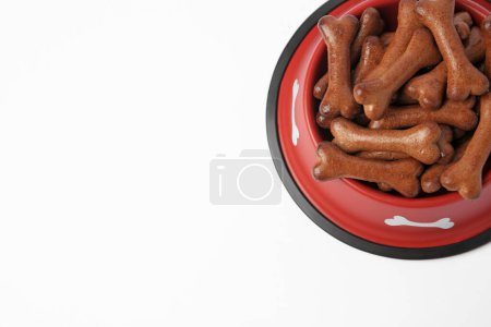 Téléchargez les photos : Bol rouge avec biscuits pour chien en forme d'os sur fond blanc, vue ci-dessus. Espace pour le texte - en image libre de droit