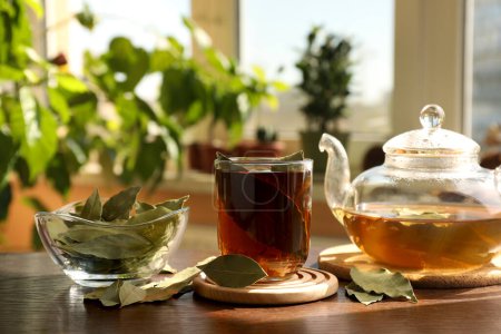 Téléchargez les photos : Tasse de thé fraîchement infusé, feuilles de laurier et théière sur table en bois à l'intérieur - en image libre de droit