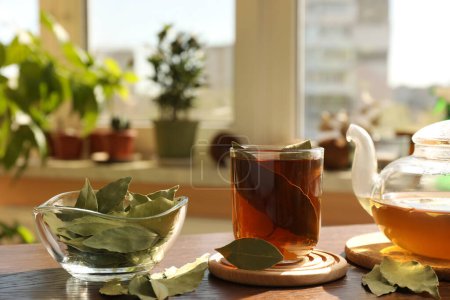 Téléchargez les photos : Tasse de thé fraîchement infusé, feuilles de laurier et théière sur table en bois à l'intérieur - en image libre de droit