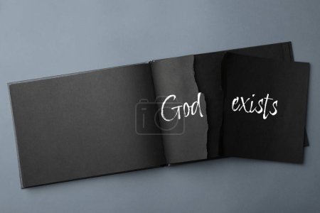 Téléchargez les photos : L'athéisme comme position religieuse. Papier déchiré avec texte Dieu Existe dans le carnet sur fond gris, vue du dessus - en image libre de droit