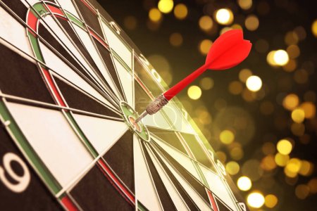 Dart board with red arrow hitting target against blurred background, bokeh effect
