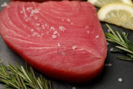 Raw tuna fillet with rosemary, sea salt and lemon slices on black table, closeup