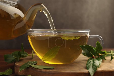 Téléchargez les photos : Verser du thé fraîchement infusé avec des feuilles de laurier dans une tasse sur une planche de bois, gros plan - en image libre de droit
