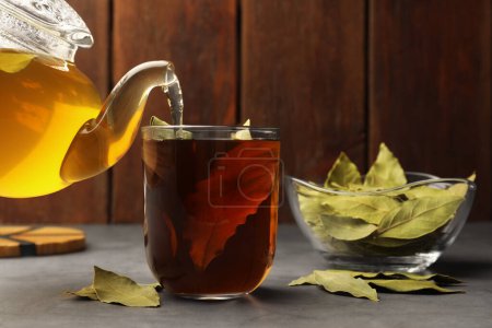 Téléchargez les photos : Verser le thé fraîchement infusé avec des feuilles de laurier dans une tasse sur une table grise - en image libre de droit