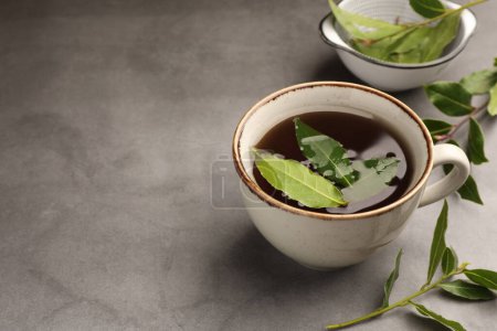 Téléchargez les photos : Tasse de thé fraîchement infusé avec des feuilles de laurier sur table grise, espace pour le texte - en image libre de droit