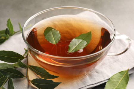 Téléchargez les photos : Tasse de thé fraîchement infusé avec des feuilles de laurier sur table grise, gros plan - en image libre de droit