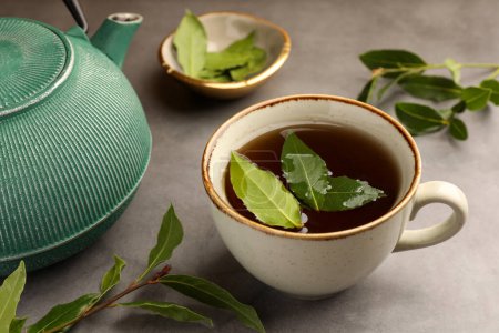 Téléchargez les photos : Coupe de thé fraîchement infusé, théière et feuilles de laurier sur table grise, gros plan - en image libre de droit