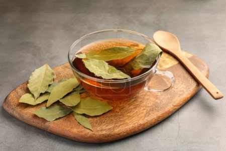 Téléchargez les photos : Tasse de thé fraîchement infusé avec feuilles de laurier sur table grise - en image libre de droit