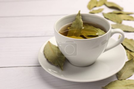 Téléchargez les photos : Coupe de thé fraîchement infusé avec des feuilles de laurier sur table en bois blanc, gros plan. Espace pour le texte - en image libre de droit