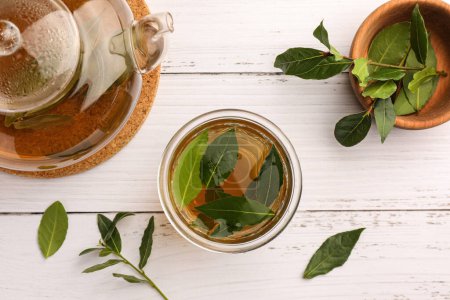 Téléchargez les photos : Coupe de thé fraîchement infusé, théière et feuilles de laurier sur table en bois blanc, plat - en image libre de droit