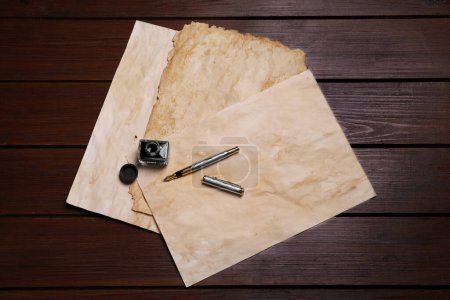Tintenfass, Füllfederhalter und Vintage-Pergament auf Holztisch, flach gelegt