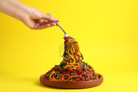 Photo for Woman eating delicious spaghetti painted with different food colorings on yellow background, closeup - Royalty Free Image