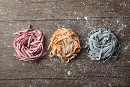 Photo for Rolled pasta painted with food colorings and flour on wooden table, flat lay - Royalty Free Image