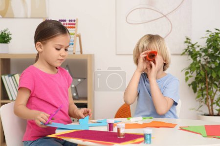 Téléchargez les photos : Enfants mignons faisant des jouets en papier au bureau dans la chambre. Lieu de travail - en image libre de droit