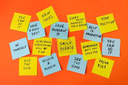 Papiernotizen mit lebensbejahenden Phrasen auf orangefarbenem Hintergrund