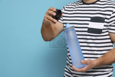 Téléchargez les photos : Homme ouvrant bouteille en plastique transparent avec de l'eau sur fond bleu clair, gros plan. Espace pour le texte - en image libre de droit