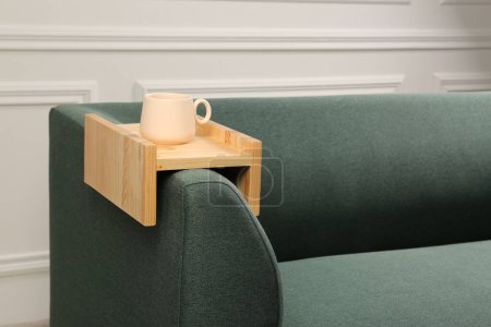 Cup of tea on sofa with wooden armrest table in room, space for text. Interior element