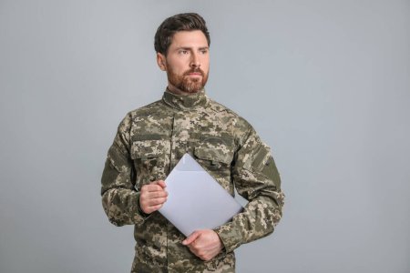 Soldat avec ordinateur portable sur fond gris clair. Service militaire