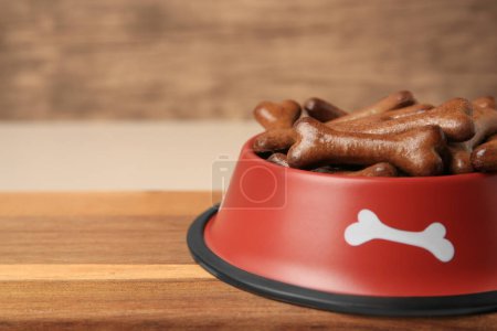 Téléchargez les photos : Bol rouge avec biscuits pour chien en forme d'os sur une planche en bois, gros plan. Espace pour le texte - en image libre de droit