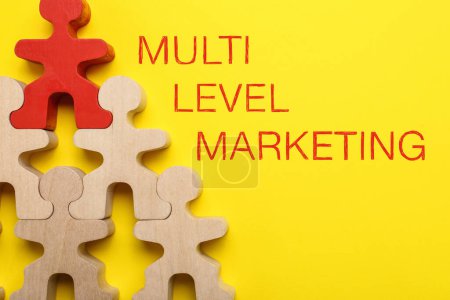 Téléchargez les photos : Marketing multi-niveaux. Pyramide de figures humaines en bois avec une rouge en haut montrant la hiérarchie sur fond jaune, couché plat - en image libre de droit